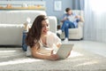 Smiling beautiful woman using laptop with blurred man in background at home Royalty Free Stock Photo