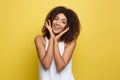 Smiling beautiful young African American woman in white T-shirt posing with hands on chin. Studio shot on Yellow Royalty Free Stock Photo