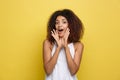 Smiling beautiful young African American woman in white T-shirt posing with hands on chin. Studio shot on Yellow Royalty Free Stock Photo