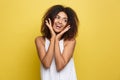 Smiling beautiful young African American woman in white T-shirt posing with hands on chin. Studio shot on Yellow Royalty Free Stock Photo