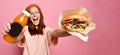 Smiling beautiful young blond woman model in hipster hoodie cloth holding hamburger and bottle juice Royalty Free Stock Photo