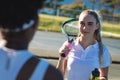 Smiling beautiful young female caucasian player looking at african american athlete at tennis court Royalty Free Stock Photo