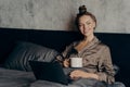 Smiling beautiful young female using laptop while lying in bed with cup of coffee Royalty Free Stock Photo