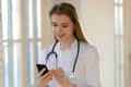 Smiling beautiful young general practitioner using smartphone. Royalty Free Stock Photo