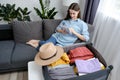 Smiling beautiful young girl sitting on cozy sofa take note and checklist, packing or prepare clothes into luggage, travel case Royalty Free Stock Photo