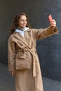 Smiling beautiful young stylish girl holding her mobile phone in a hand and making a selfie photo Royalty Free Stock Photo