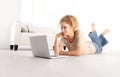 smiling beautiful young woman with computer laptop, lying on living room wooden floor in modern comfortable white home Royalty Free Stock Photo