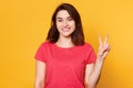 Smiling beautiful young woman dressed casually, showing two fingers or victory gesture, isolated over yellow background, has happy Royalty Free Stock Photo