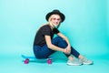 Smiling beautiful young woman sitting and posing on skateboard over green background Royalty Free Stock Photo