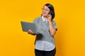 Smiling beautiful young woman talking on smartphone and looking at laptop screen on yellow background Royalty Free Stock Photo