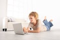 smiling Beautiful young woman using a laptop, lying on living room wooden floor in modern white home Royalty Free Stock Photo