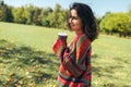 Smiling beautiful young woman wearing sweater and holding disposable cup of coffee in the city park. Pretty female student Royalty Free Stock Photo