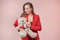 Smiling beautyful woman in a red jacket lovingly looks at a toy bear in the image of Santa Claus