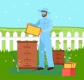 Smiling beekeeper in blue protect suit collecting honeycombs near two hives at bee-garden