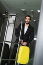 smiling bellboy carrying luggage near metallic