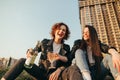 Smiling best friends girls drink wine on a walk. Portrait of two happy girls romantically sitting on lawn on cityscape background Royalty Free Stock Photo
