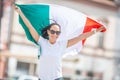 Smiling beuatiful girl in sunglasses and white t-shirt holds Italian flag on a street celebrating