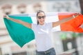 Smiling beuatiful girl in sunglasses and white t-shirt holds Italian flag on a street celebrating