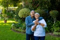 Smiling biracial senior couple embracing and looking up while standing against plants in park Royalty Free Stock Photo