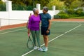 Smiling biracial senior couple with rackets looking at each other while standing at tennis court Royalty Free Stock Photo