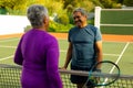 Smiling biracial senior husband talking with senior wife while playing tennis at tennis court Royalty Free Stock Photo