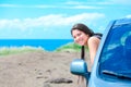 Smiling biracial teen girl leaning out car door by ocean