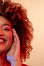 Smiling biracial woman with curly hair in pink eyeshadow and lipstick touching face in red light Royalty Free Stock Photo