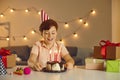 Smiling birthday boy in festive cap sitting and looking at birthday cake with candles Royalty Free Stock Photo
