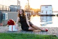 Smiling birthday girl with brown hair in little black dress sitting on the wooden footpath at sunset Royalty Free Stock Photo