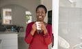 Smiling Black African woman standing, home doorway holding coffee cup