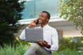 Smiling black businessman using laptop and talking on cellphone while sitting outdoors Royalty Free Stock Photo