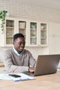 Smiling black businessman working remotely from homeoffice on laptop computer.