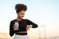 Smiling Black Female Jogger Checking Running Time On Smartwatch After Outdoor Training