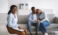 Smiling black female psychologist and young married couple hugging after successful marital therapy at office Royalty Free Stock Photo