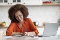 Smiling Black Freelancer Woman Working With Laptop In Kitchen And Taking Notes Royalty Free Stock Photo