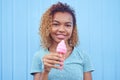 Smiling black girl with pink melting ice cream at blue wall background