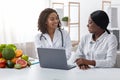 Smiling black lady doctor with female patient at clinic