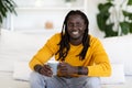 Smiling black man with cup of coffee relaxing on couch at home Royalty Free Stock Photo