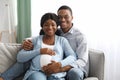 Smiling black man hugging his pregnant woman, sitting on sofa Royalty Free Stock Photo