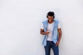 Smiling black man leaning against wall with smart phone and headphones Royalty Free Stock Photo