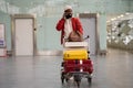 Smiling Black man pushing luggage trolley walking after arrival at airport, talking on mobile phone. Royalty Free Stock Photo