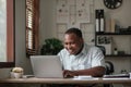 Smiling black man using laptop at home in living room. Happy mature businessman send email and working at home. African Royalty Free Stock Photo