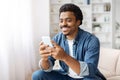 Smiling Black Man Using Smartphone in Bright Living Room Royalty Free Stock Photo