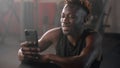 smiling black man is using smartphone in gym, after workout, portrait of african athlet