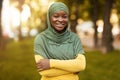 Smiling Black Muslim Woman In Hijab Standing With Folded Arms Outdoors