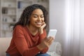 Smiling Black Woman Reading Message On Smartphone While Sitting On Couch Royalty Free Stock Photo