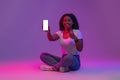 Smiling black woman sitting on floor and showing smartphone with blank screen Royalty Free Stock Photo