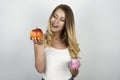 Smiling blond attractive woman holding juicy red apple in one hand and pink tasty cupcake in other hand isolated white Royalty Free Stock Photo