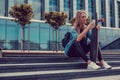 Smiling blond female sitting on staps and using smartphone.