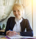 Smiling blond haired female student sitting in audience, writing and looking at camera Royalty Free Stock Photo